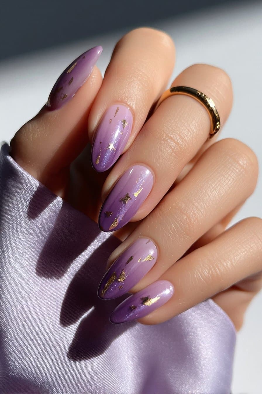Amethyst almond nails with glossy purple base and scattered gold foil accents, full hand with fingers curved inward.