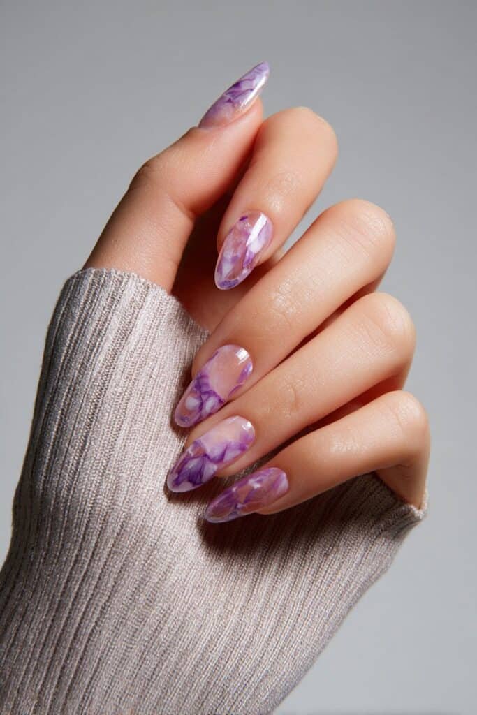 Amethyst watercolor almond nails with soft lavender and violet brushstroke blend, full hand with fingers curved inward.