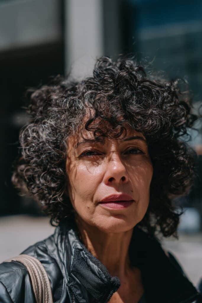older woman with curly undercut, short sides and voluminous top curls, chest-length portrait