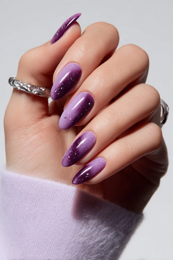 Twilight sky amethyst almond nails with deep purple gradient and tiny star-like sparkles on a full hand with fingers curved inward.