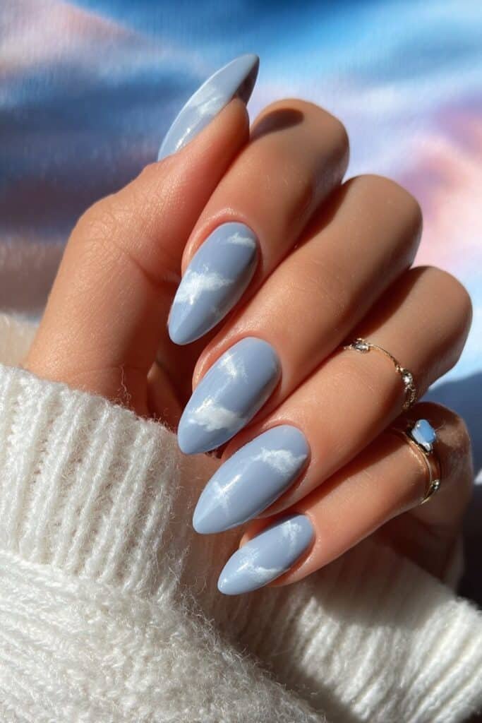 Baby blue almond nails with fluffy white cloud designs.