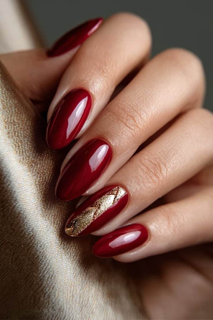 Deep red nails with elegant gold accents and metallic detailing.