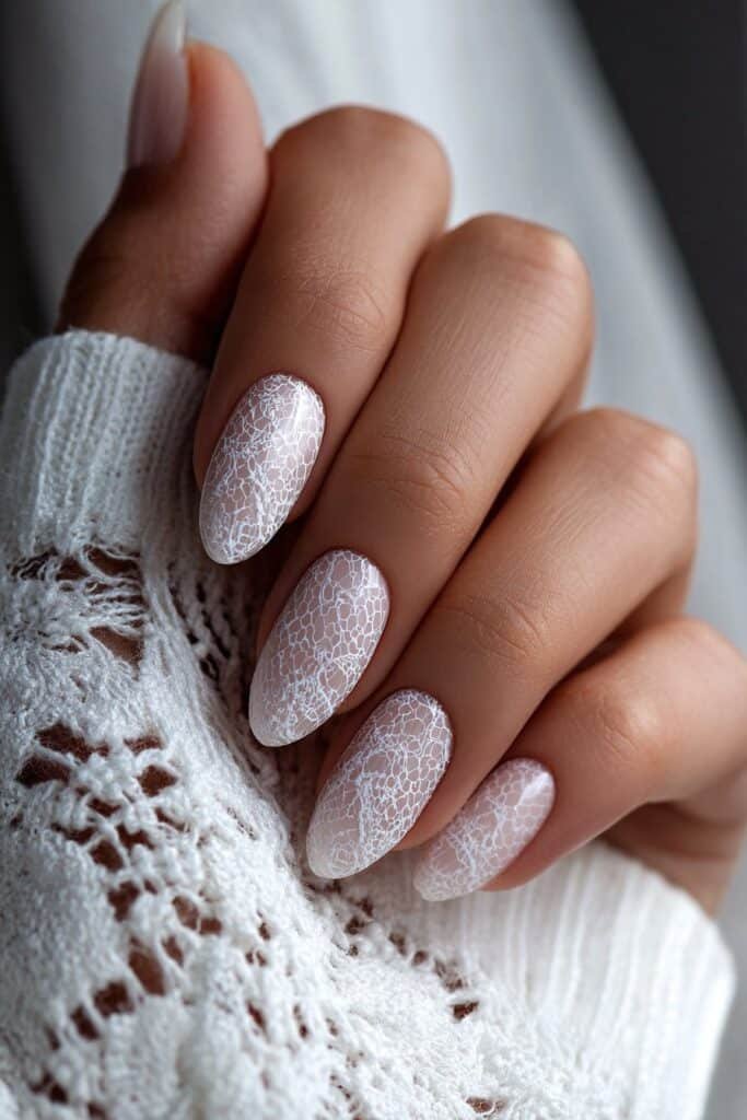 Almond nails with intricate white lace detailing.