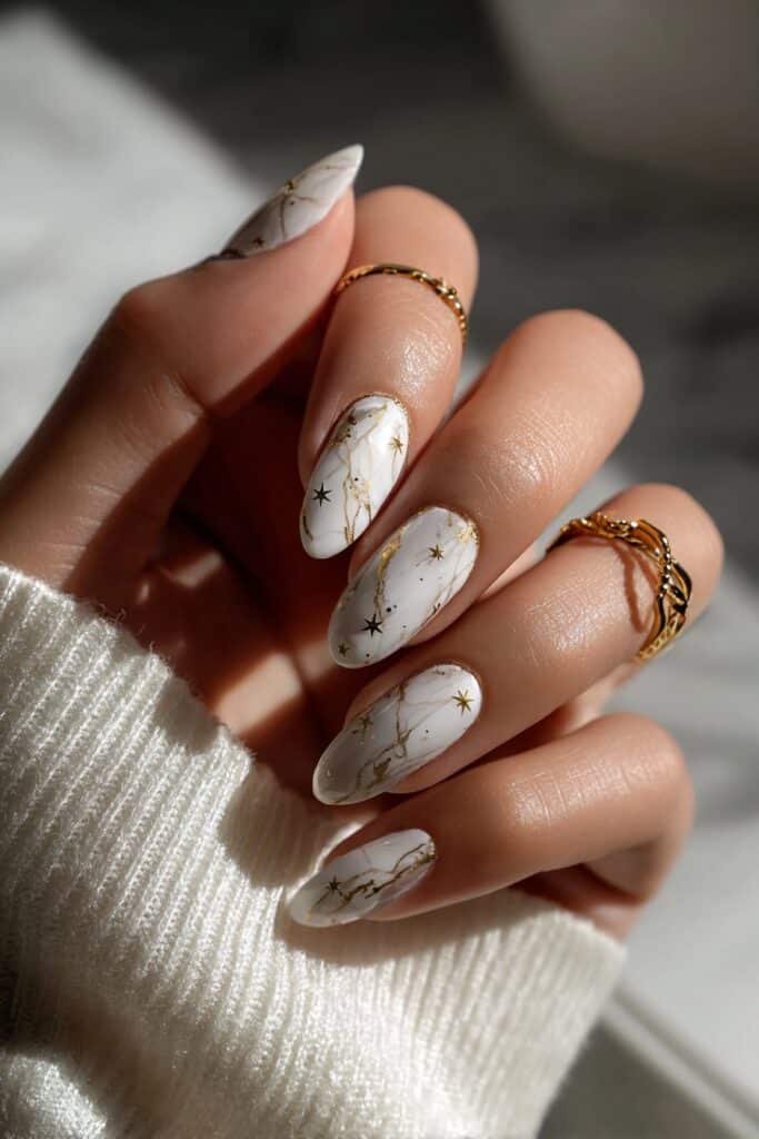 White marble nails with gold star accents and swirl details.