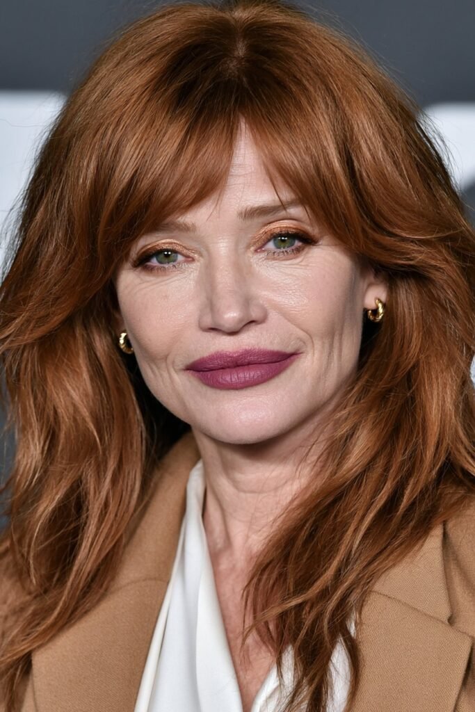 Woman over 60 with feathered layers and soft curtain bangs in auburn hair.