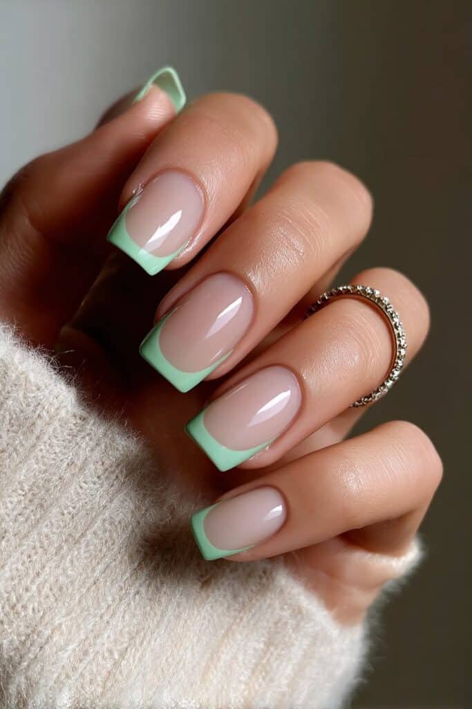 Square nails with mint green French tips on nude base.