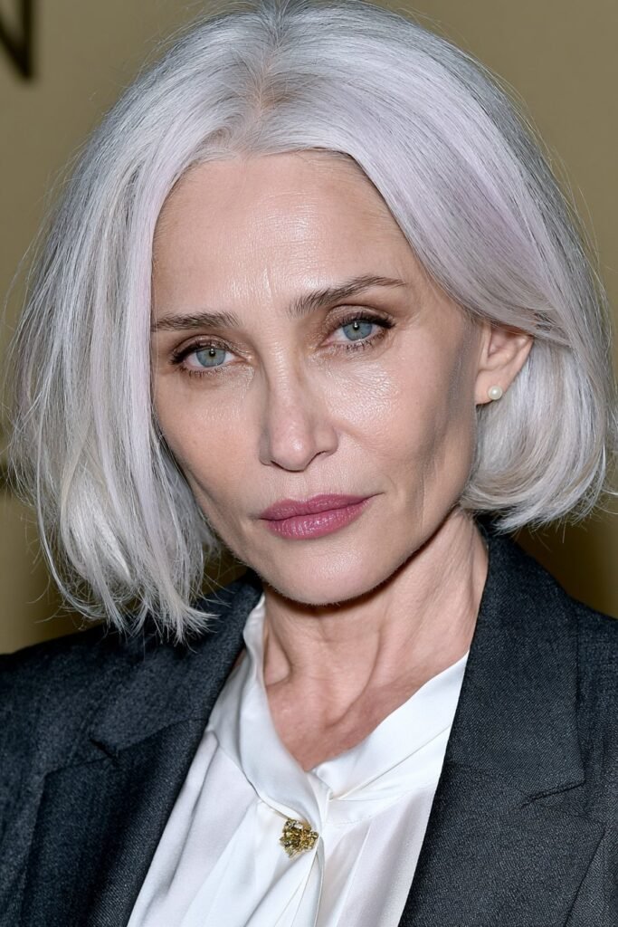 Elegant woman with a warm chestnut layered bob, charcoal blazer, and soft ivory studio background.