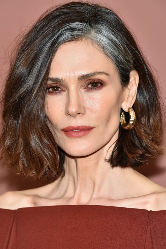 Stylish woman with a tousled brunette textured lob and rust-toned off-shoulder top in a terracotta studio.