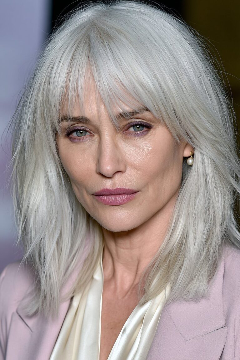 Graceful woman with wispy bangs and an ash blonde layered lob in a soft lavender studio portrait.