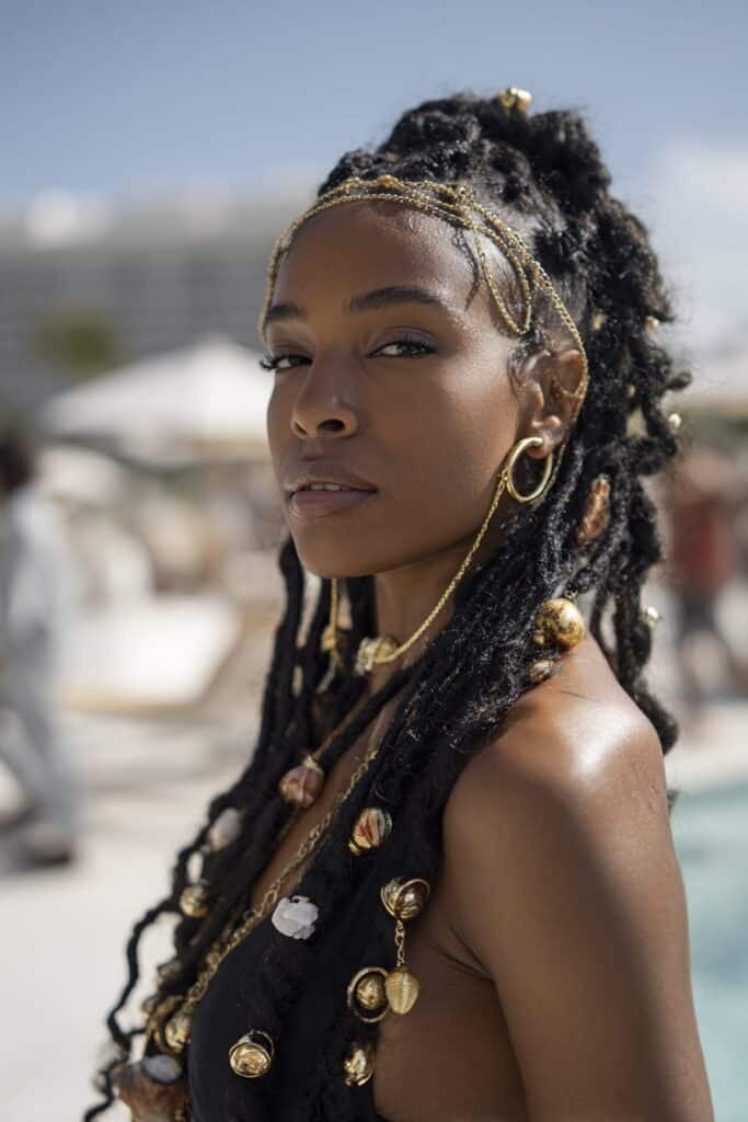 Black woman with kinky twists decorated with gold cuffs and beads.