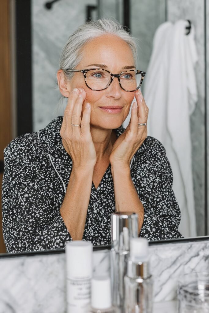 Older woman wearing glasses applying primer before mekup application.