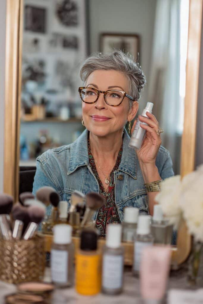 Older woman wearing glasses finishing her makeup with a hydrating setting mist.
