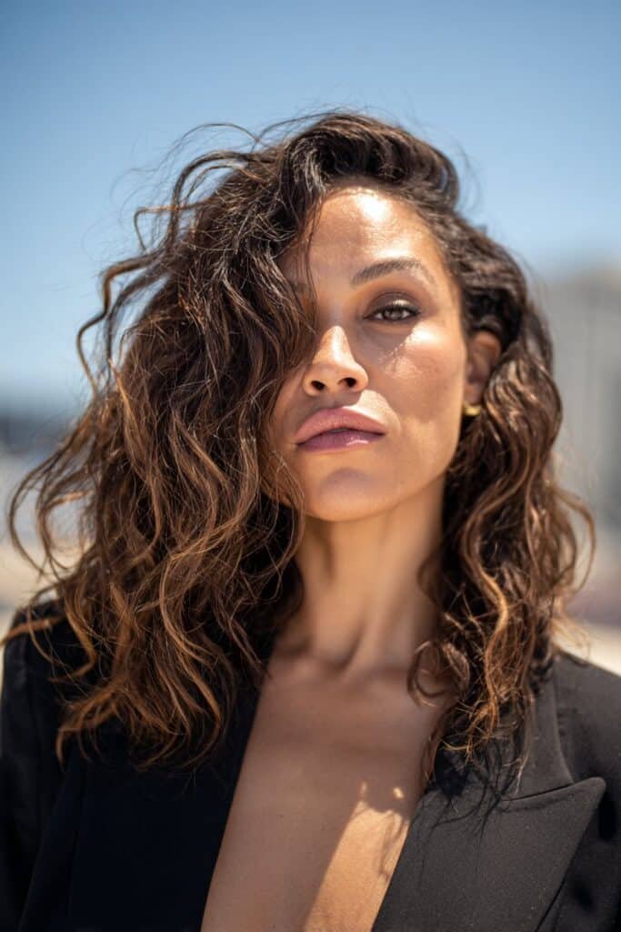 Woman with textured shoulder-length beach waves and a dramatic deep side part.