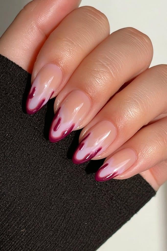 Short almond nails with deep blood-red dripping French tips over sheer nude bases.