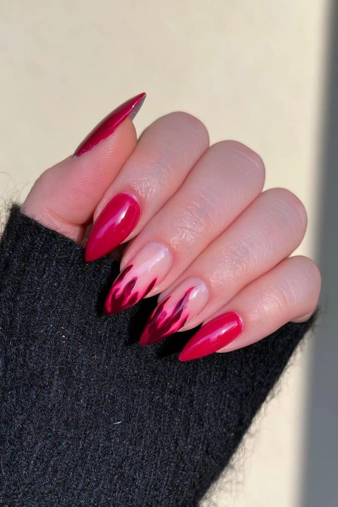 Short red and nude almond nails with one stylized dark-red handprint accent.