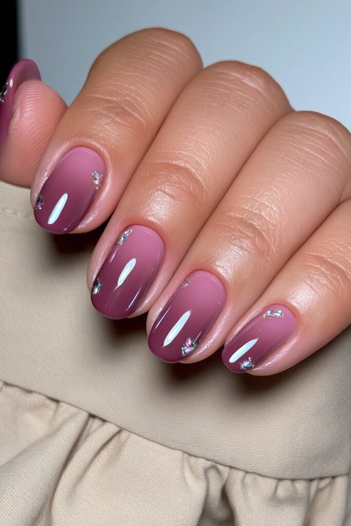 Short burgundy nails with elegant gems accent details.