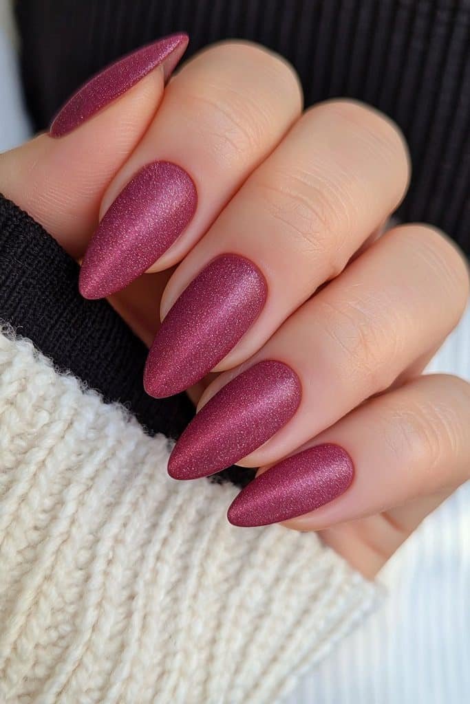 Short almond nails in deep burgundy velvet with luminous cat-eye shimmer.