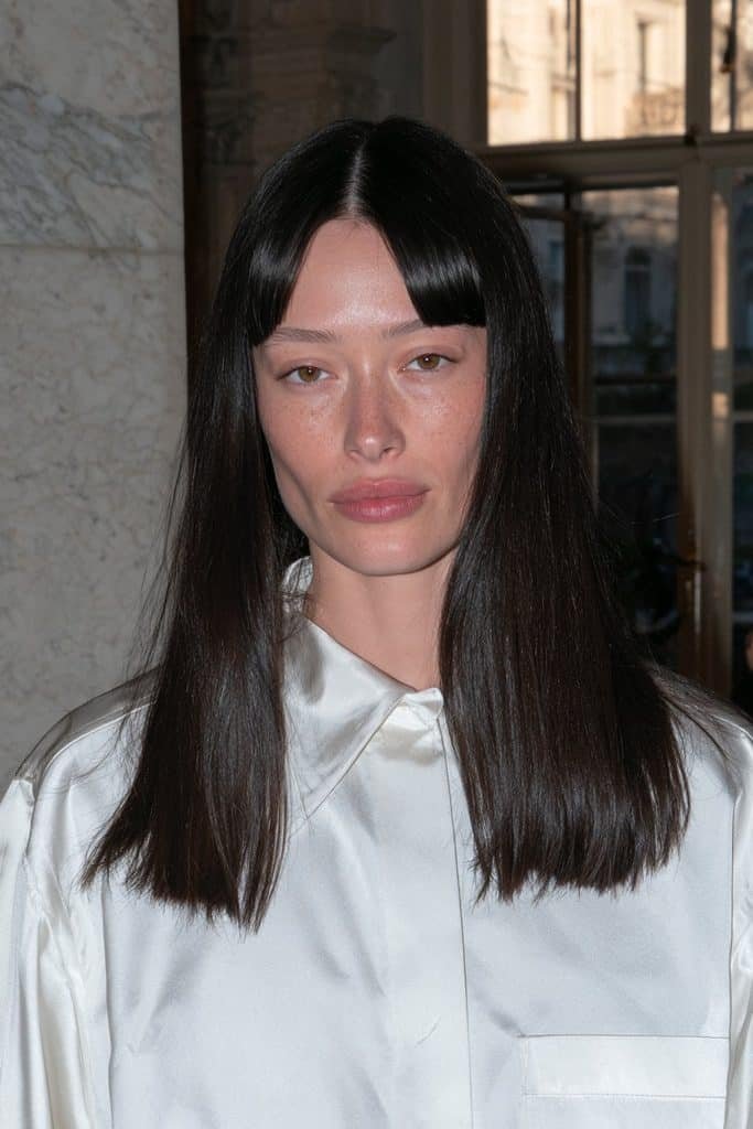 Young woman with a sleek center-part jellyfish haircut in glossy jet-black hair.