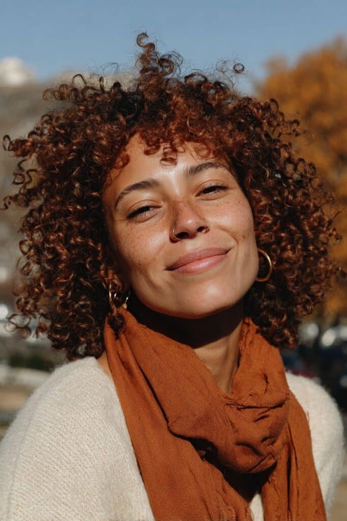 Black woman with voluminous cinnamon-colored crochet curls and warm autumn tones.