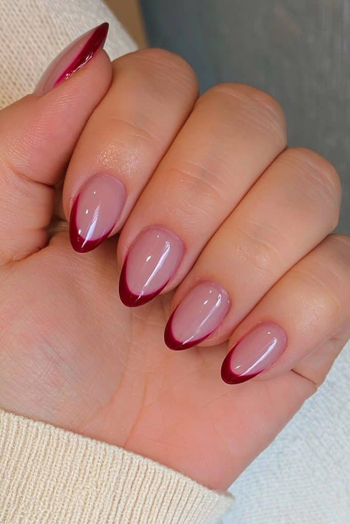 Cranberry red French tip Thanksgiving nails on short almond nails with a glossy nude base.