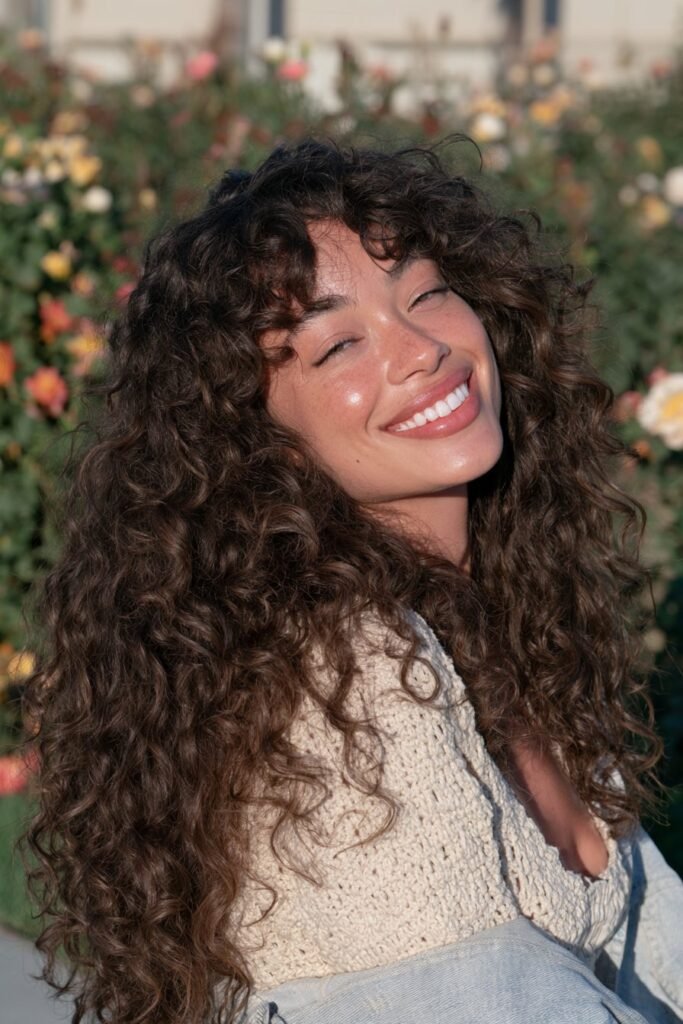 Long curly brunette wolf haircut with a textured crown, layered curls, face-framing pieces, and tapered ends.