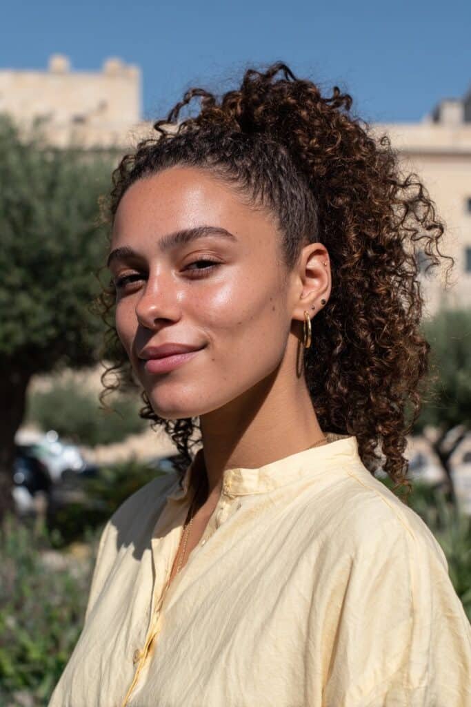 Woman in her 20s with a high curly ponytail and face-framing tendrils