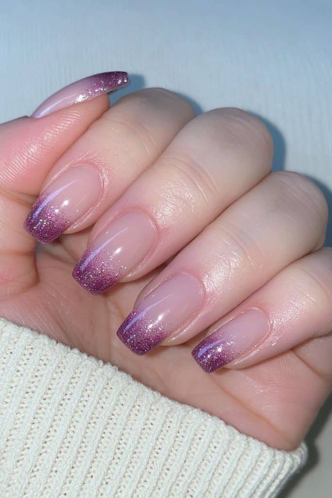 Short nude nails with sparkling amethyst purple glitter French tips.
