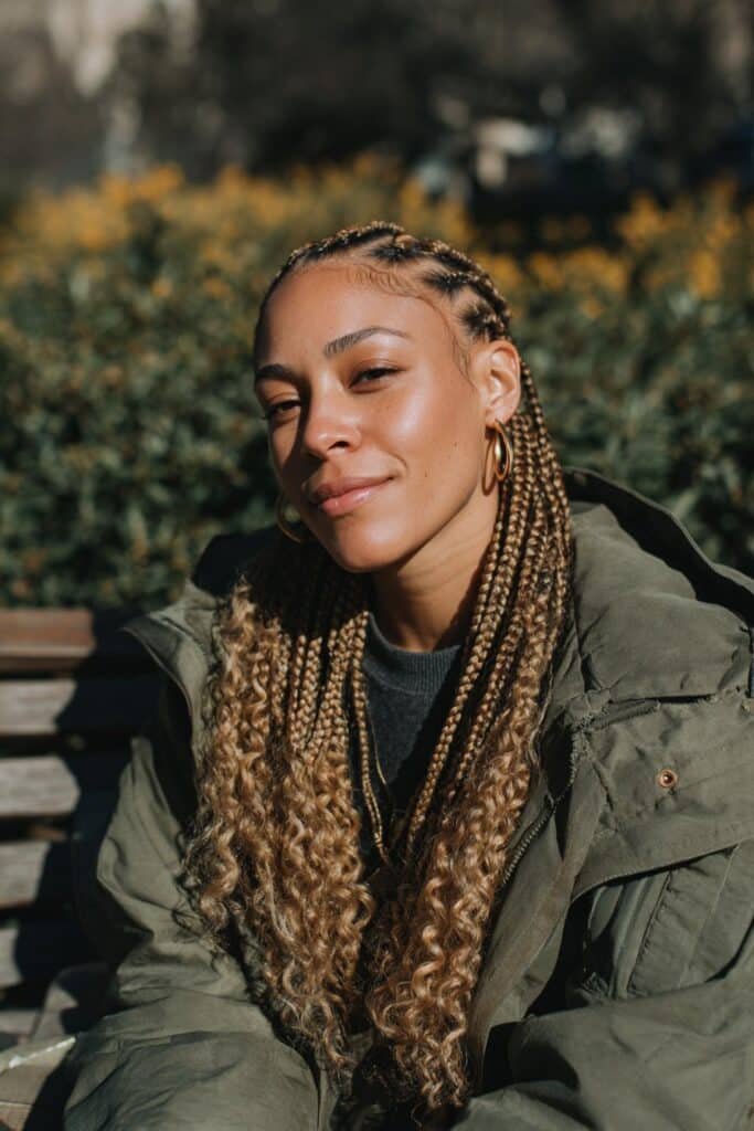 Black woman wearing long honey-blonde goddess braids with curly tendrils.