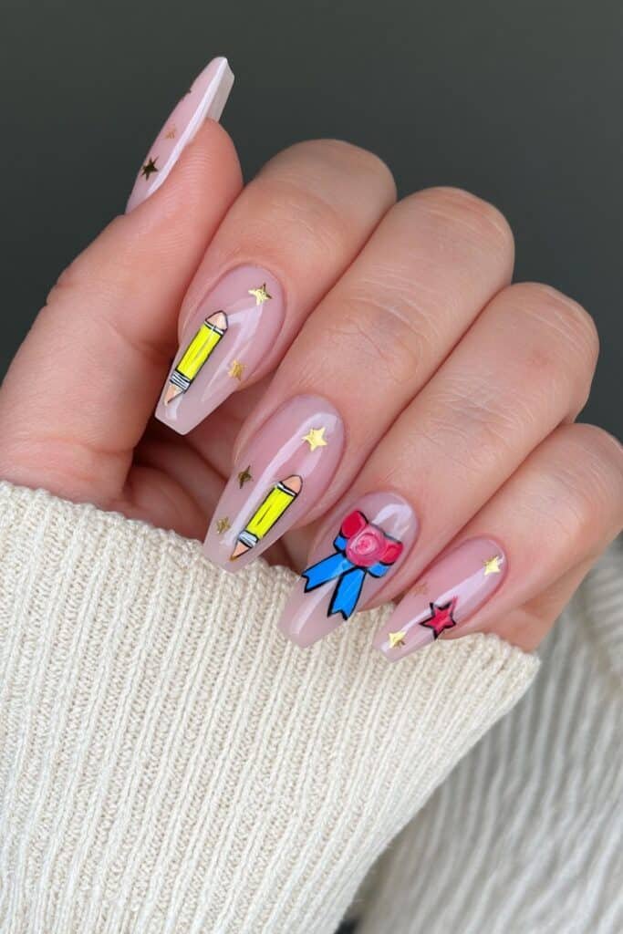 Nude pencil-themed nails with gold stars and an honor roll ribbon accent.