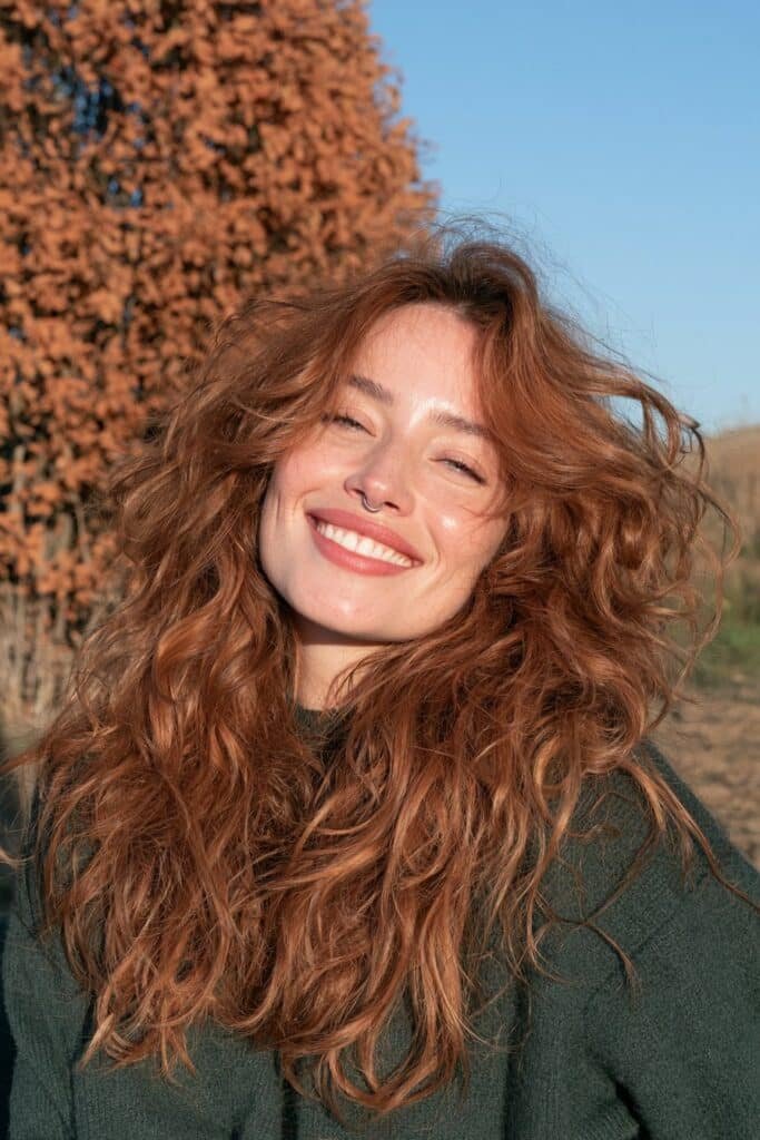 Long vibrant copper-red wolf haircut with choppy textured layers, voluminous crown, and flowing feathered ends.