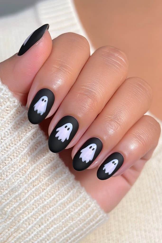 Short Halloween nails with matte black polish and tiny white ghost accents.