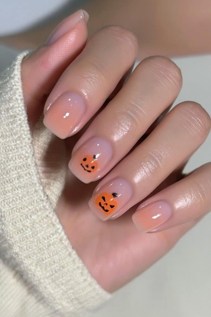 Short milky nude nails with tiny orange pumpkins face accent.