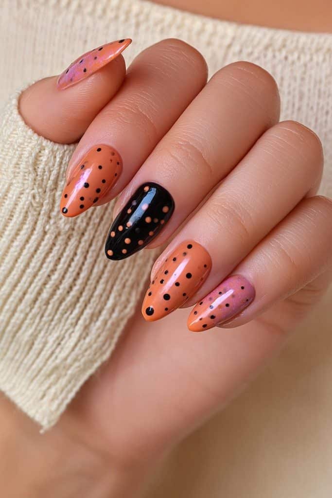 Short orange and black almond nails with playful contrasting dot accents.
