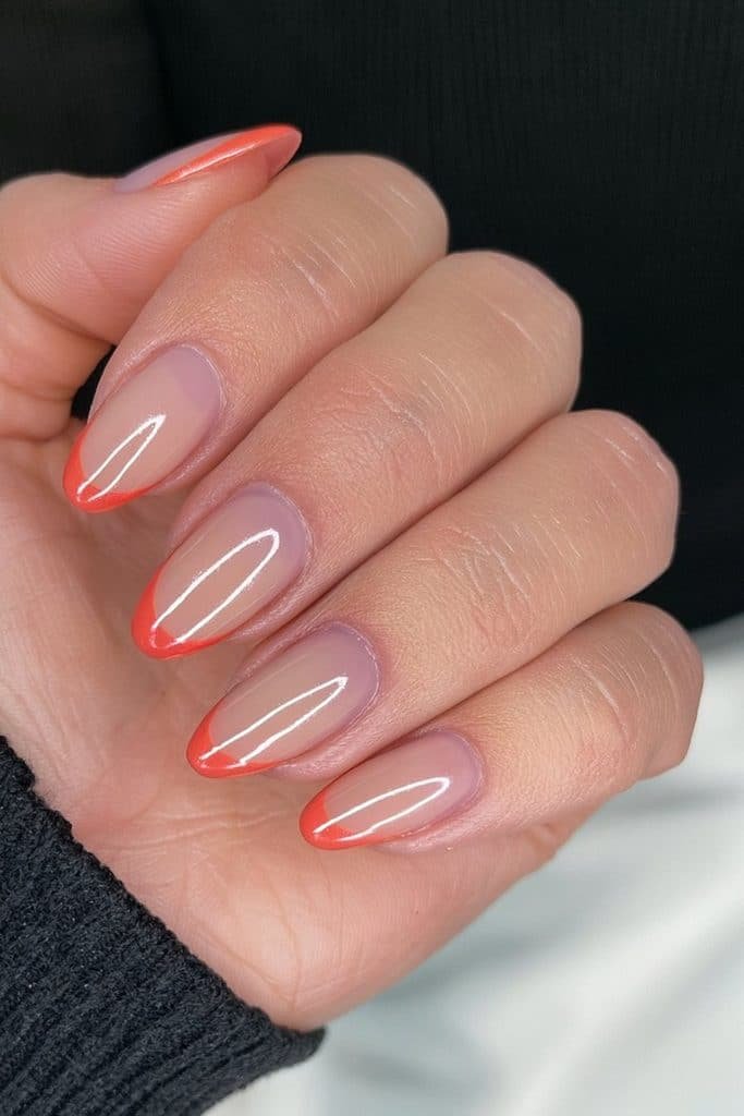 Short nude nails with vivid orange chrome French tips.