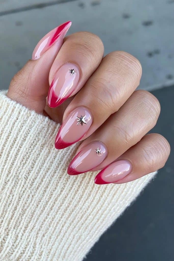Short nude almond nails with scarlet French tips and tiny star charms.