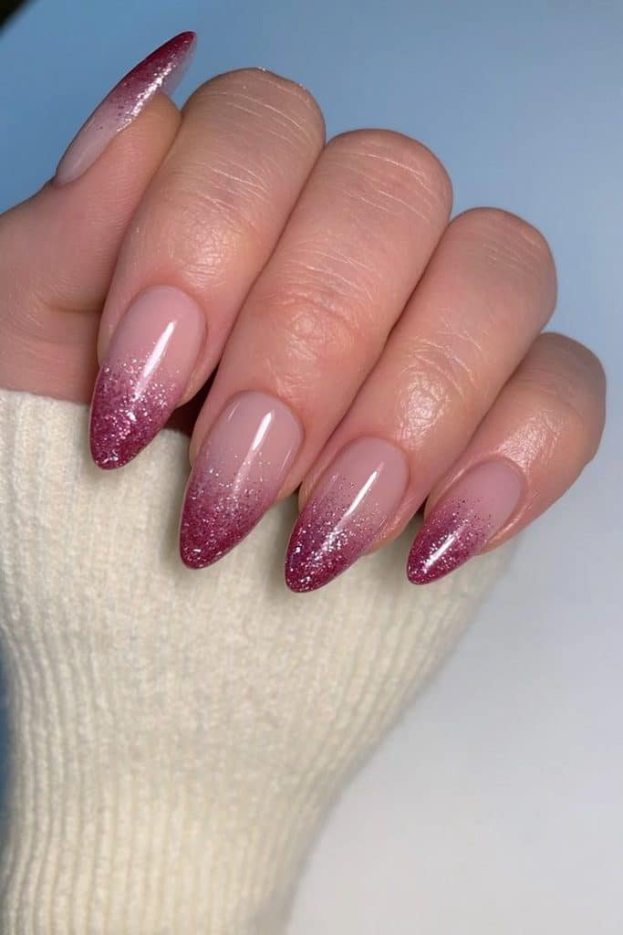 Short almond nails with sparkling ruby-red glitter fading from the tips.
