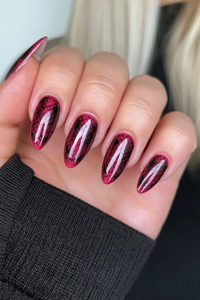 Short crimson almond nails with black snakeskin scale detailing.