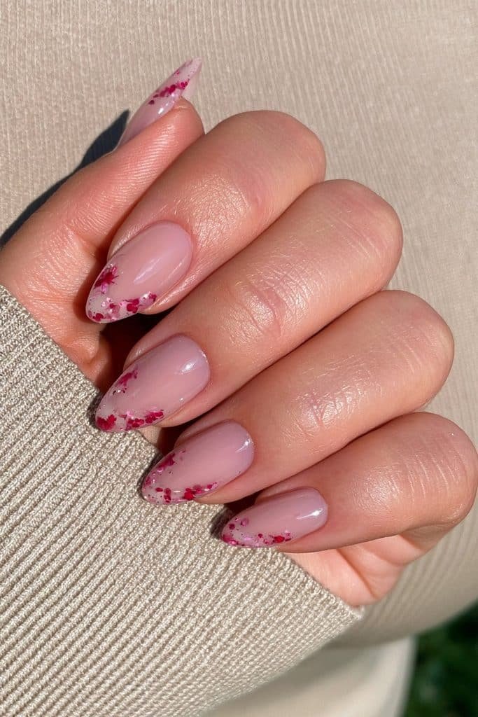 Short begie almond nails with controlled crimson-red splatter accents.