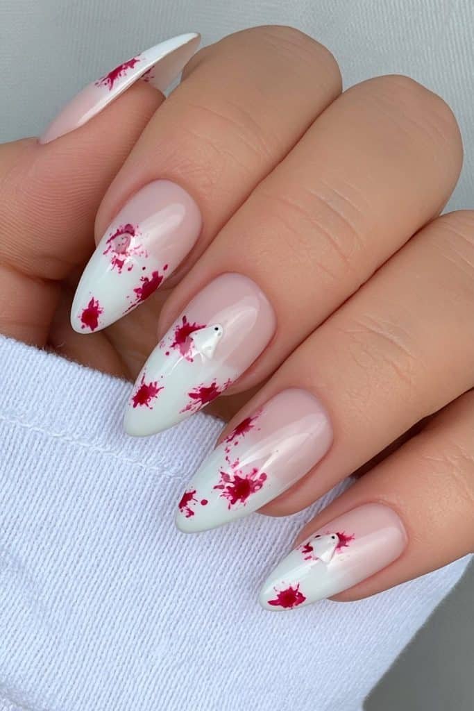 Short white almond nails with deep red splatter and tiny ghost-inspired details.