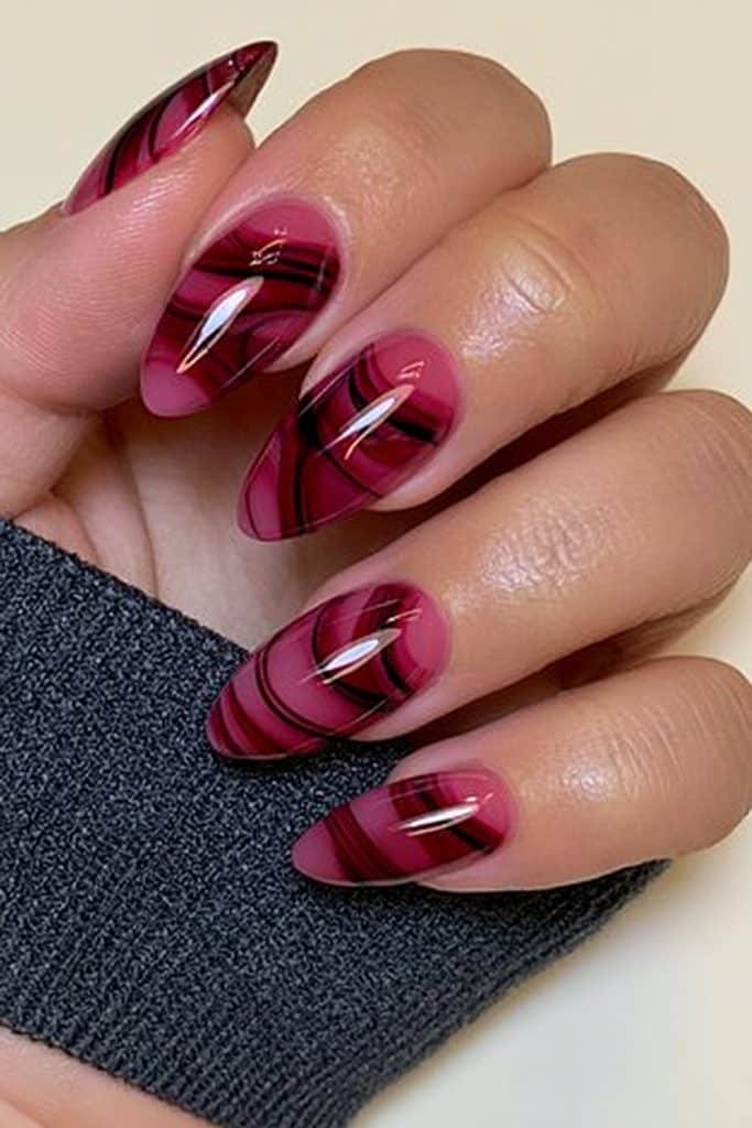 Short almond nails with crimson red and black marble swirls.