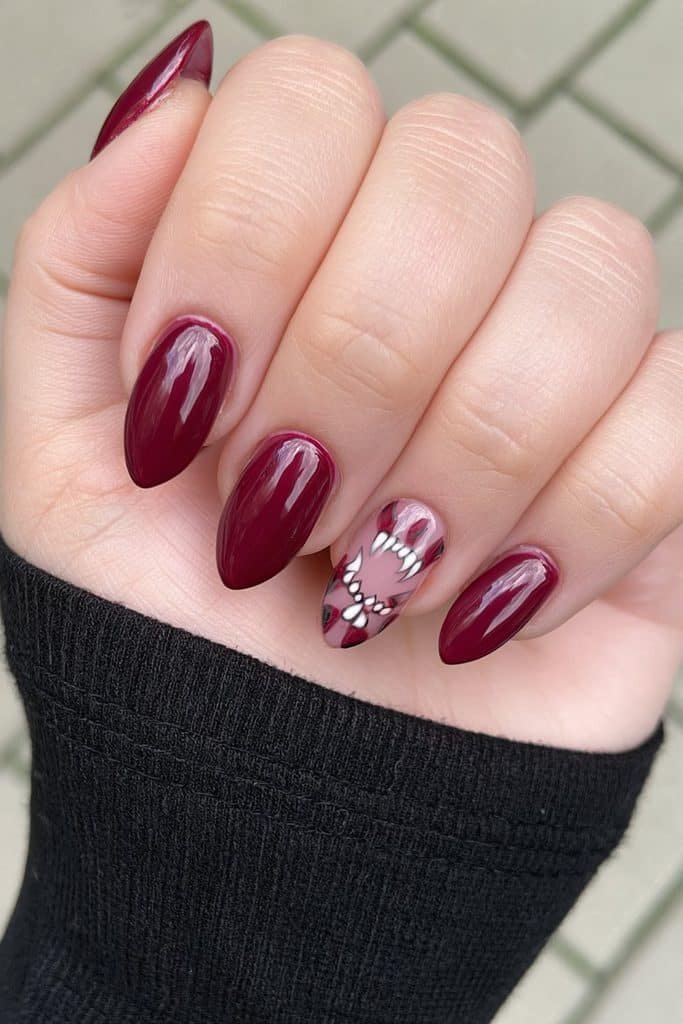 Short scarlet almond nails with one tiny white vampire fang accent.
