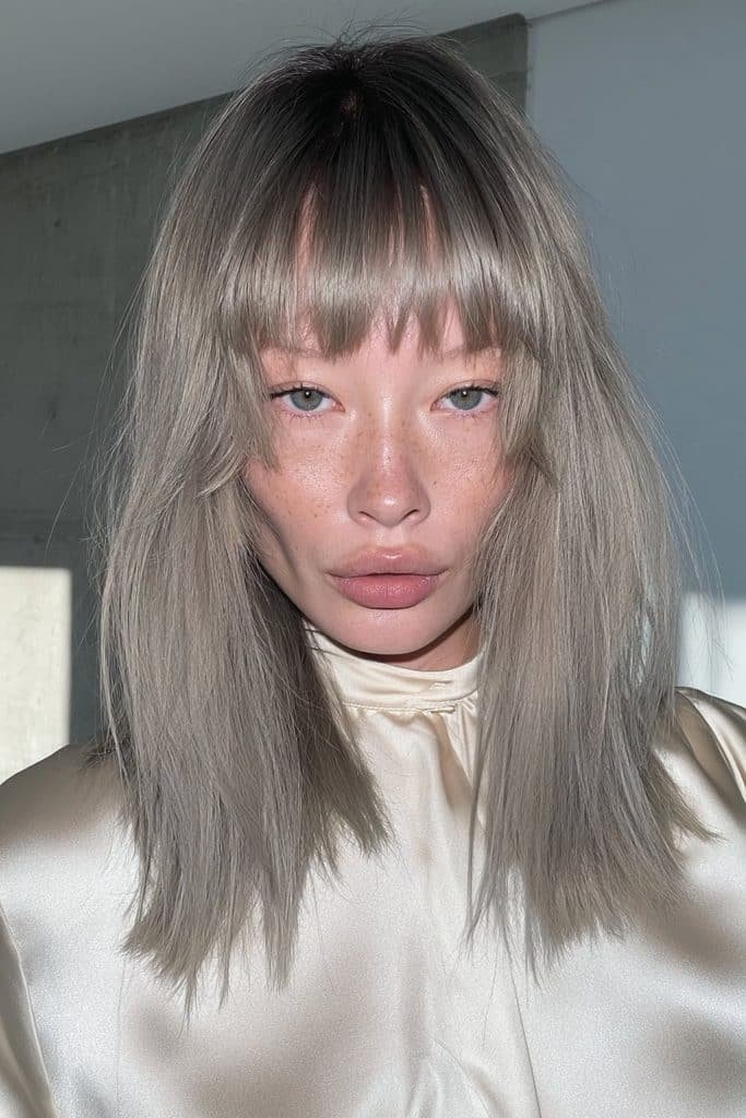 Young woman with a sleek silver and grey jellyfish haircut and glossy straight layers.