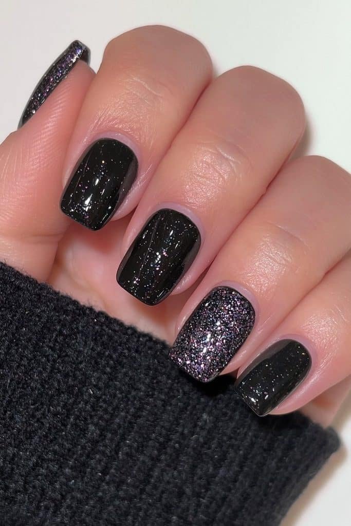 Short glossy black nails with one sparkling glitter accent nail.