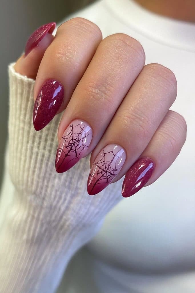 Short red almond nails with one delicate black spiderweb accent.