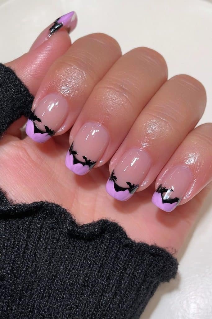 Short nails with lavender French tips and tiny bat accents.