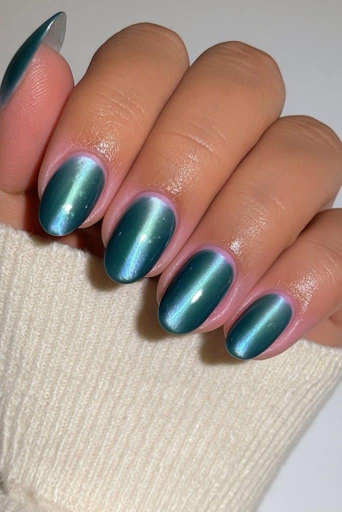 Short round nails with nude and teal velvet polish and one luminous teal accent.