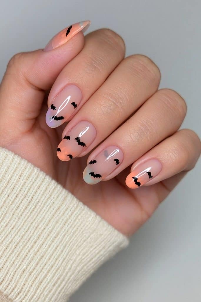Short nude nails with tiny black bat silhouette accents.