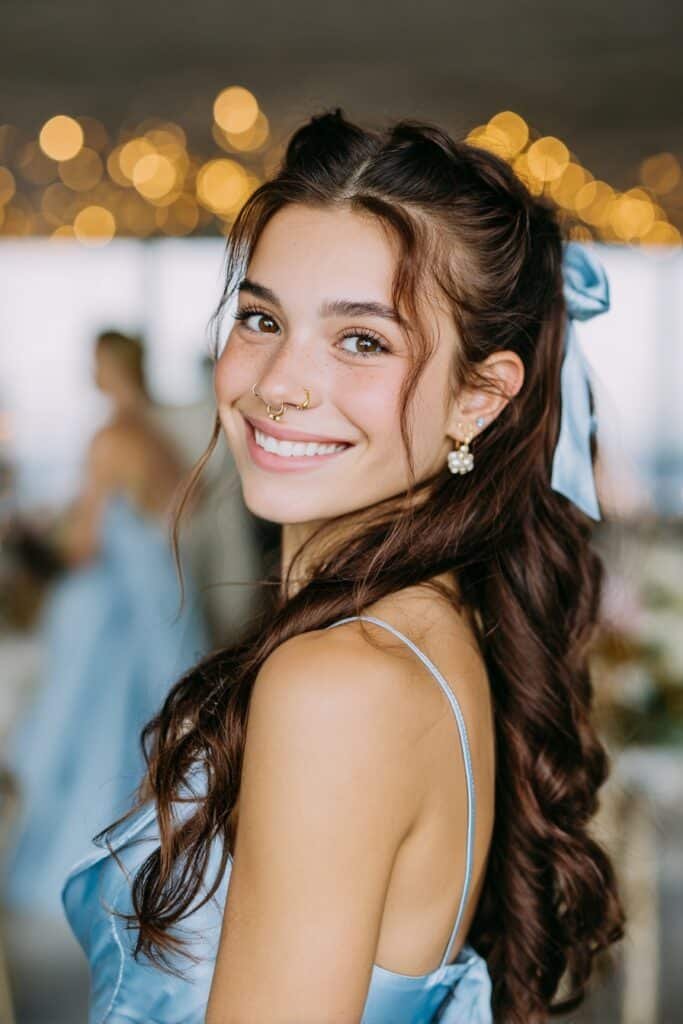 Twisted half-up hairstyle with loose curls and a satin bow accessory for a soft romantic homecoming look.