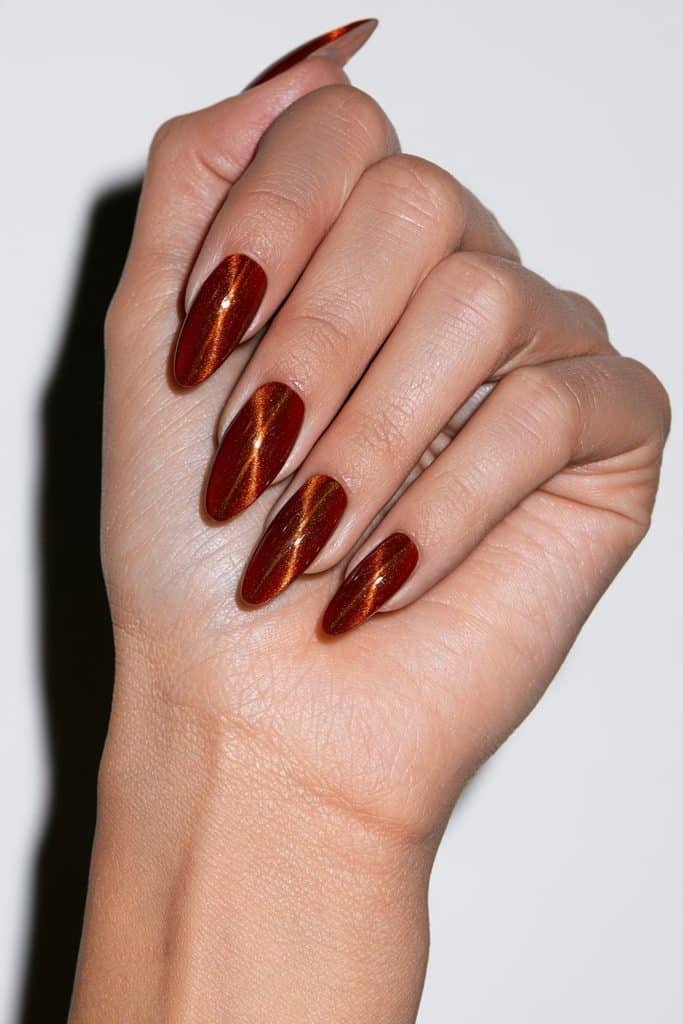 Almond-shaped orange cat eye nails with an elongated magnetic shimmer streak.