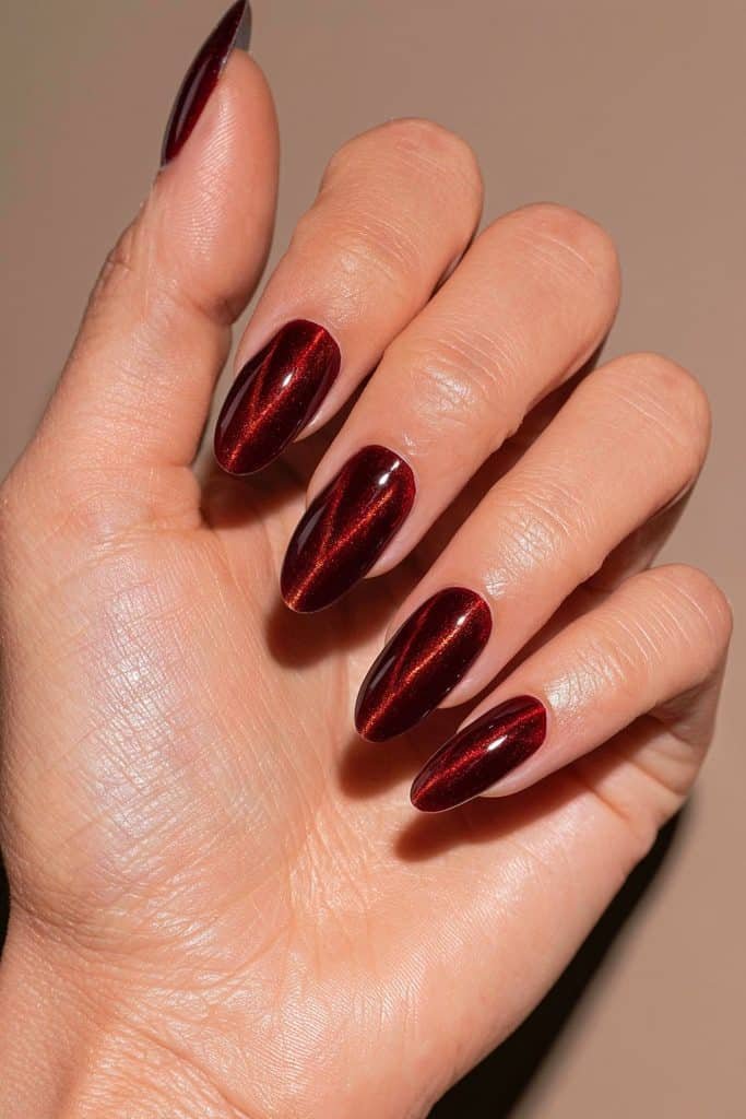 Maroon cat eye nails with a sheer wine-colored jelly layer over bronze magnetic polish for a warm metallic glow.